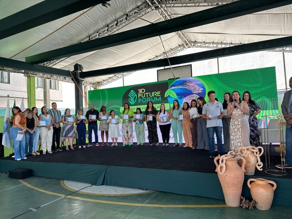 Grupo de participantes em pé no palco segurando certificados durante evento do 3D Future Forum, com painel digital ao fundo.