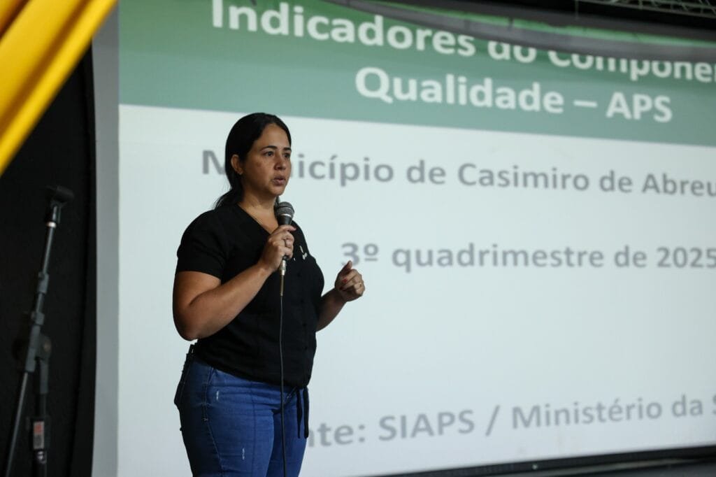 Grupo de profissionais da saúde reunidos no Cineteatro Meus Oito Anos durante capacitação do Projeto Imuniza + Brasil, em Casimiro de Abreu, com participantes levantando as mãos em momento de integração da atividade.