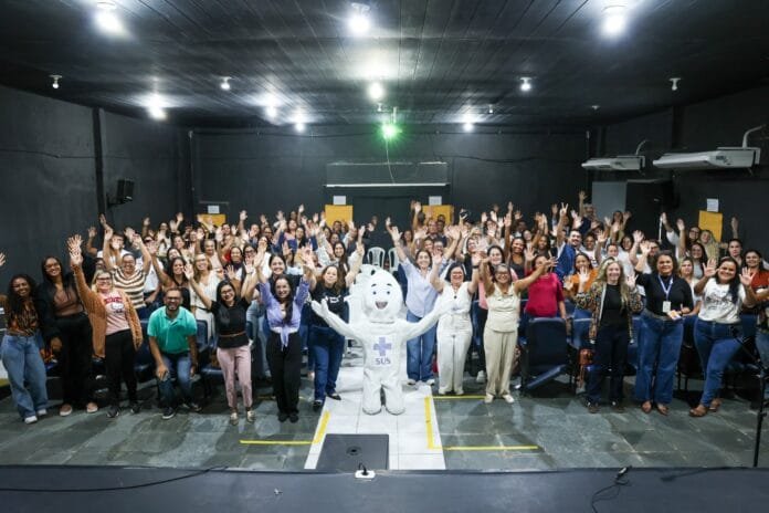 Casimiro de Abreu projeto Imuniza + Brasil 2 Grupo de profissionais da saúde reunidos no Cineteatro Meus Oito Anos durante capacitação do Projeto Imuniza + Brasil, em Casimiro de Abreu, com participantes levantando as mãos em momento de integração da atividade.