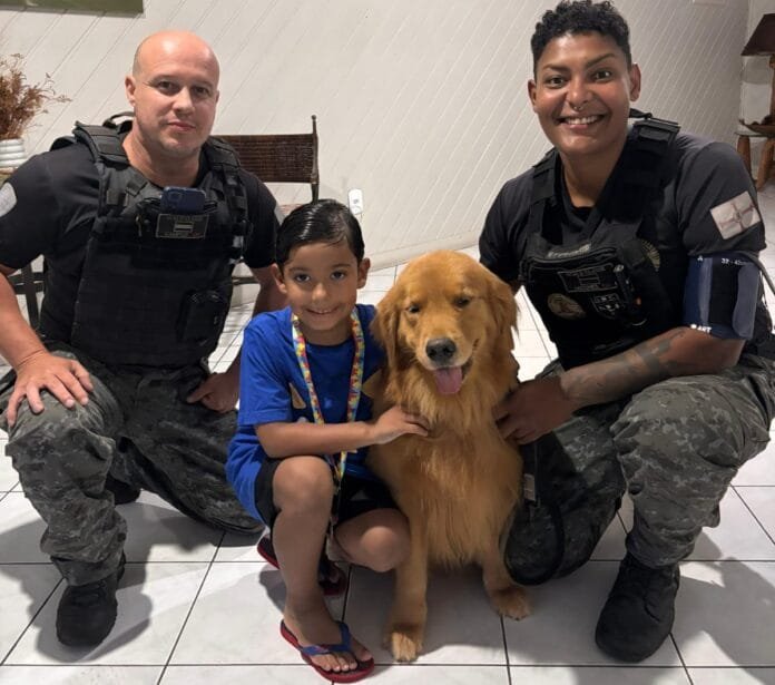 Entre sorrisos e abraços, Nicolas vive um momento de conexão e acolhimento ao lado de Bonnie, a cadela do GOC de Arraial do Cabo, acompanhada pelos agentes da equipe.