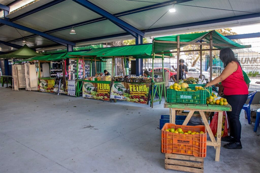 Vista externa da nova cobertura da Feira da Agricultura Familiar de Macaé com estrutura moderna e visitantes circulando pelo local.